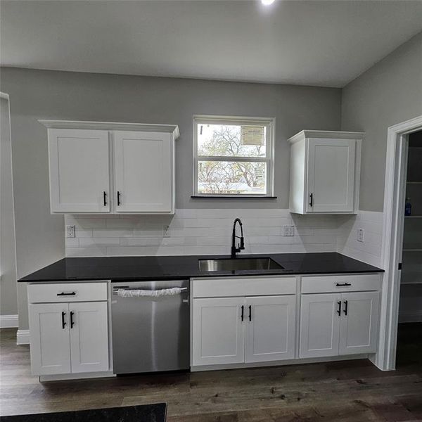 stainless steel dishwasher, white cabinets, dark wood-style floors, dark stone countertops, and backsplash