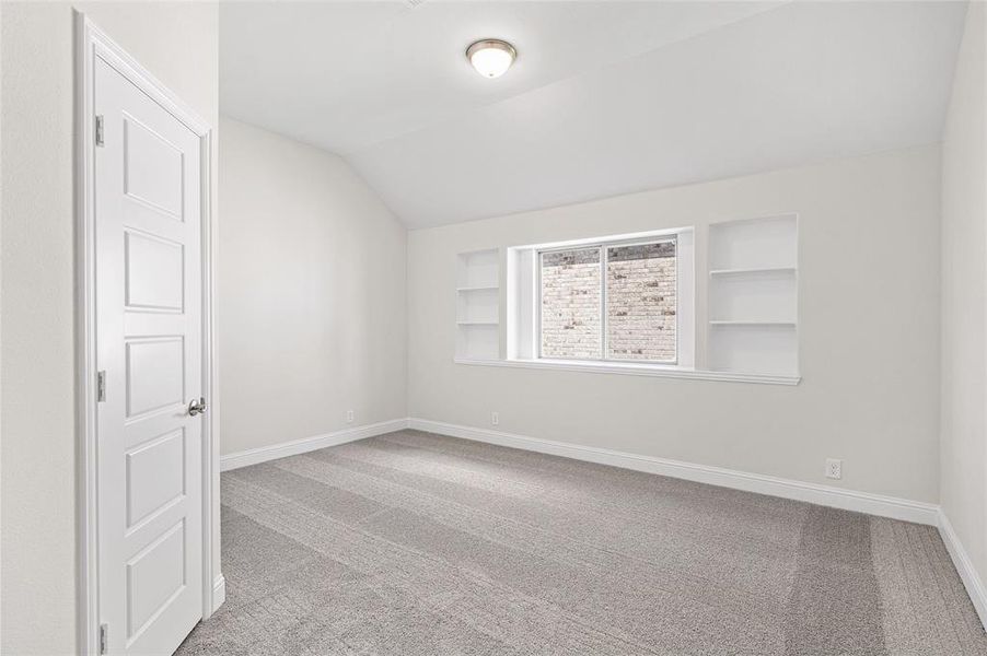 Unfurnished room with built in shelves, light carpet, and vaulted ceiling Unfurnished room with built in shelves, light carpet, and vaulted ceiling