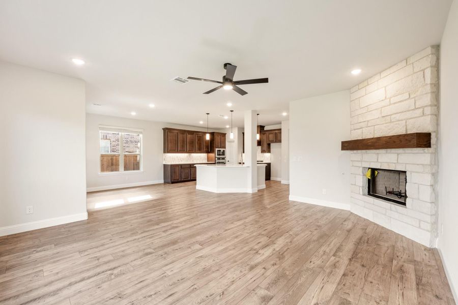 Open living area with wood floors, stone fireplace, and open-concept kitchen with dark cabinets in background