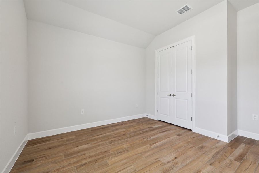 Unfurnished bedroom featuring wood finished floors, vaulted ceiling, and a closet