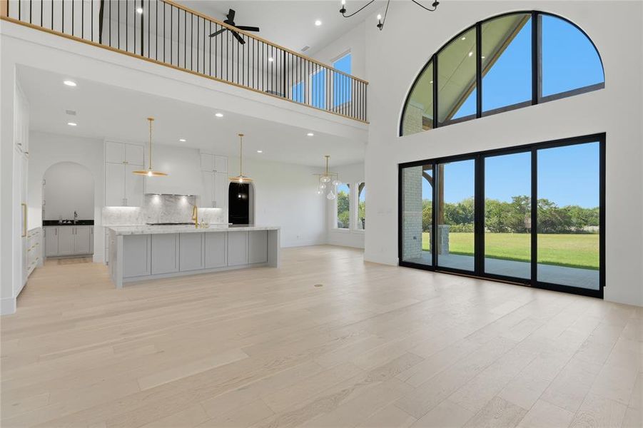 Expansive living area with light wood-finish flooring, soaring ceilings, and a second-story balcony featuring a black spindle railing