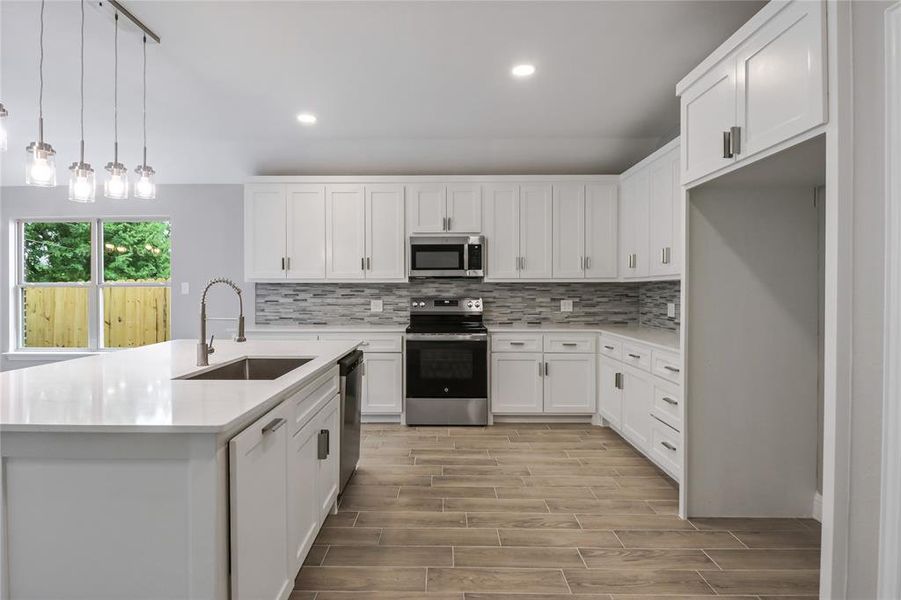 Kitchen with sink, white cabinets, backsplash, and stainless steel appliances