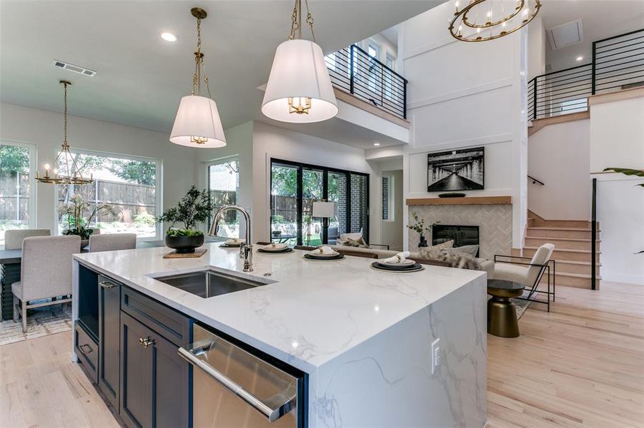 Kitchen with light hardwood / wood-style flooring, dishwasher, a tiled fireplace, a kitchen island with sink, and sink