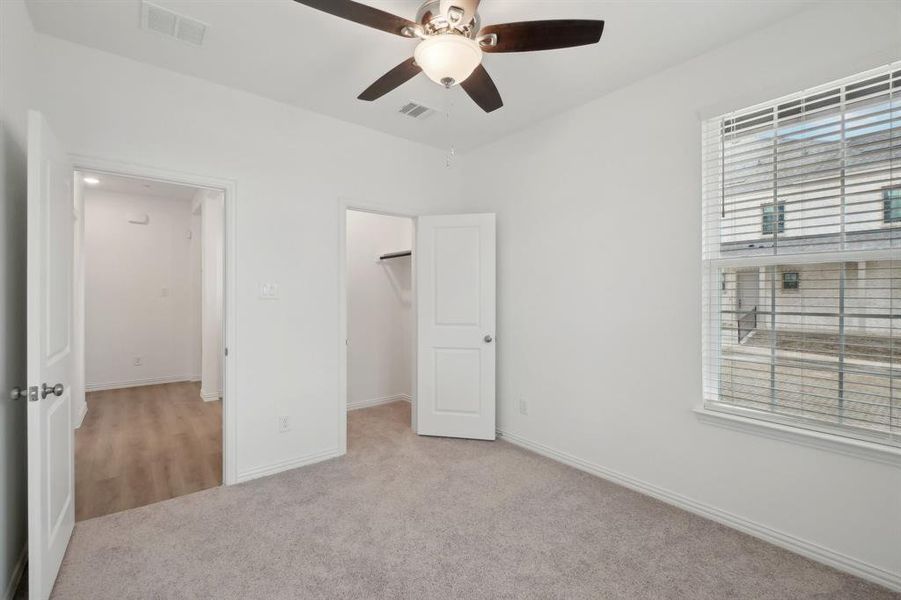 Unfurnished bedroom with a closet, a walk in closet, light colored carpet, and ceiling fan