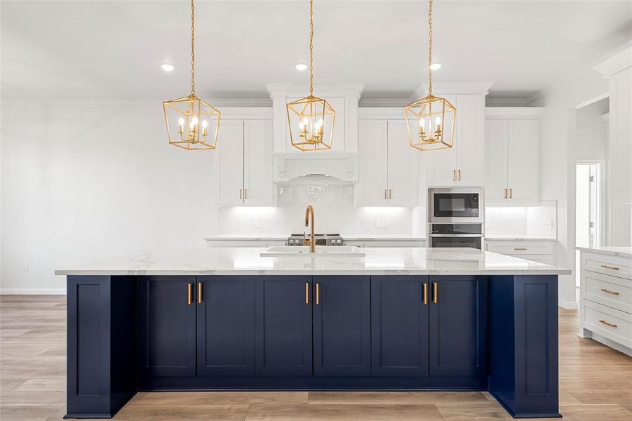 Kitchen featuring blue cabinetry, backsplash, white cabinetry, an island with sink, and crown molding