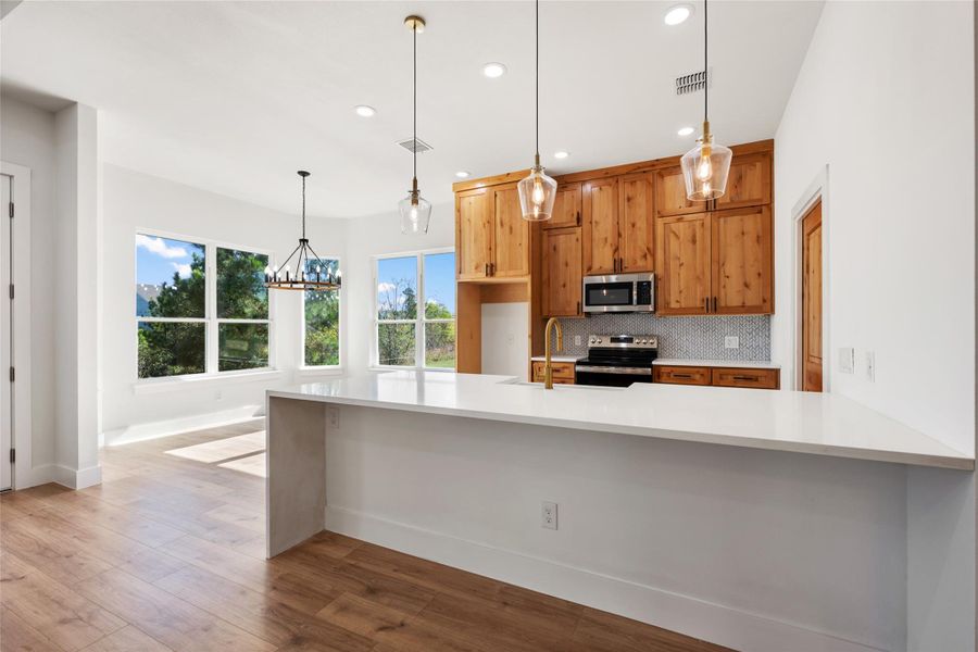 Kitchen featuring backsplash, appliances with stainless steel finishes, decorative light fixtures, light stone countertops, and recessed lighting