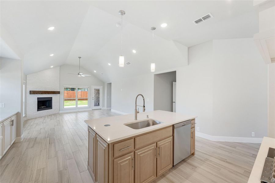 Kitchen island with sink and wood cabinets open to living room with vaulted ceiling and fireplace
