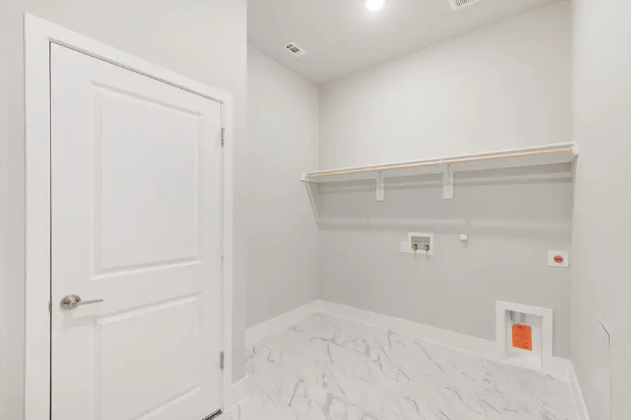 Laundry room with marble tile floor, wall shelf, washer and dryer hookups, and white door