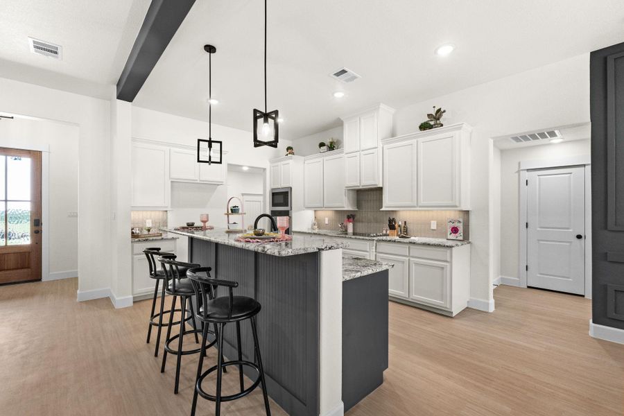 Dual tone kitchen with light stone counters, a breakfast bar area, hanging light fixtures, light wood-style floors, and a center island with sink