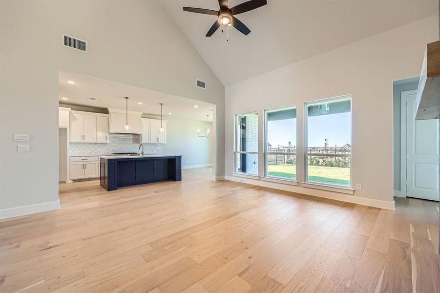 Unfurnished living room featuring ceiling fan, light hardwood / wood-style floors, sink, and high vaulted ceiling