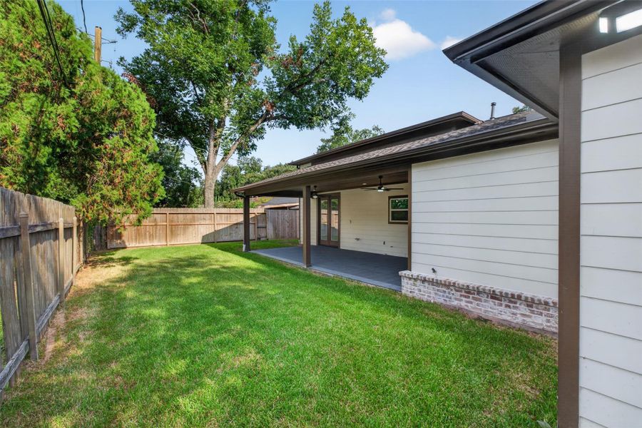 Charming backyard features a spacious covered patio, perfect for outdoor entertaining, with lush green lawn and privacy fencing.