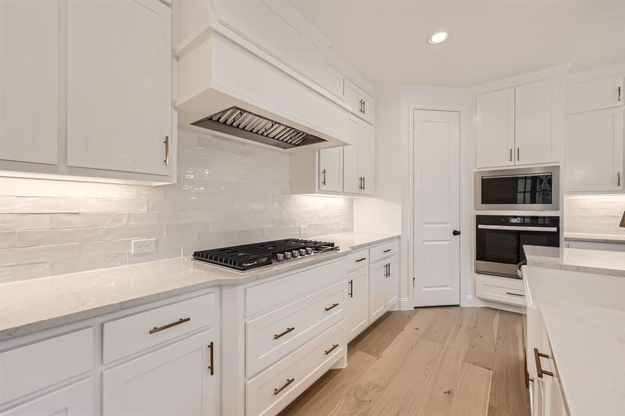 Kitchen with light hardwood / wood-style floors, white cabinetry, decorative backsplash, stainless steel appliances, and premium range hood