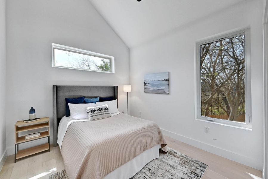 Bedroom featuring baseboards, lofted ceiling, and light wood-style flooring