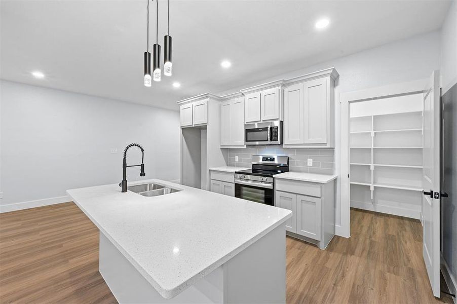 Kitchen featuring white cabinetry, sink, an island with sink, decorative light fixtures, and appliances with stainless steel finishes