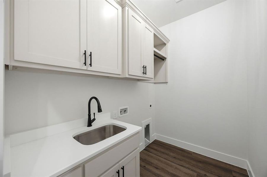 Utility room featuring white cabinetry with black hardware, a stainless steel sink with a matte black faucet, and wood-finish flooring