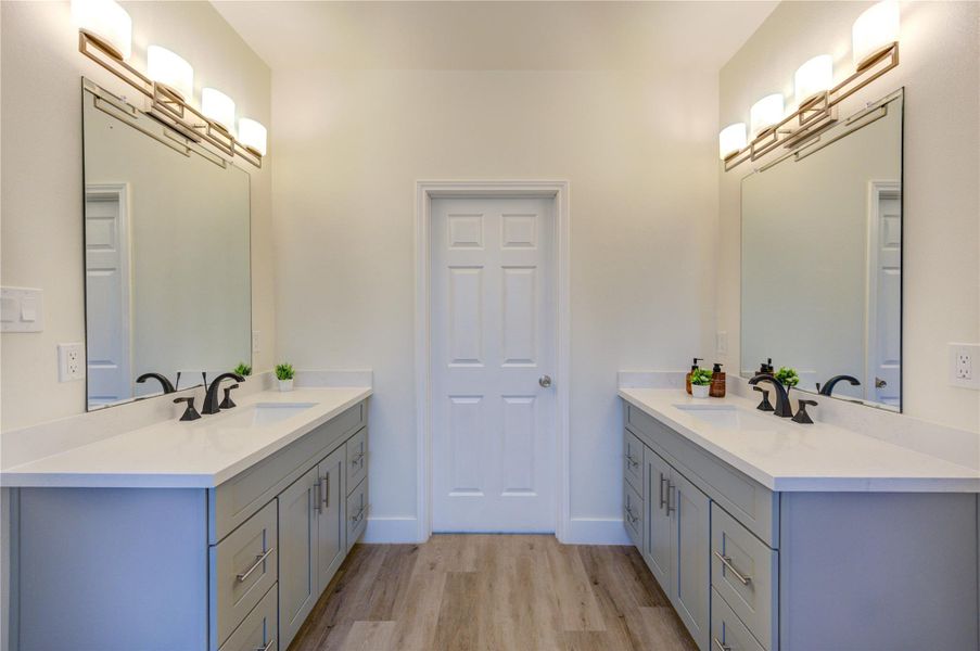 This stylish bathroom boasts a dual vanity with modern fixtures, generous storage, large mirrors, and elegant lighting, all set against a neutral palette with wood-look flooring.