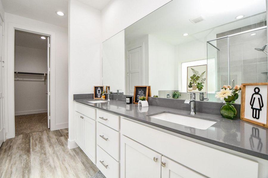 This modern bathroom features a sleek design with a large mirror, dual sinks on a quartz countertop, and white cabinetry. The space includes a frameless glass-enclosed shower and connects to a walk-in closet, offering both functionality and style. This modern bathroom features a sleek design with a large mirror, dual sinks on a quartz countertop, and white cabinetry. The space includes a frameless glass-enclosed shower and connects to a walk-in closet, offering both functionality and style.