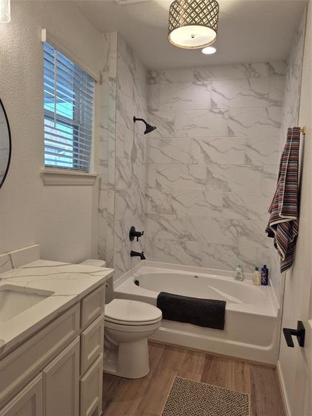 Full bathroom featuring vanity, shower / bath combination, light wood-style flooring, and a textured wall