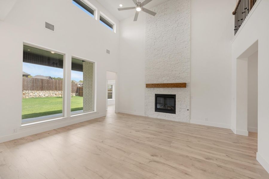 Open living room with two-story ceiling, white stone fireplace, wood mantel, and light hardwood floors