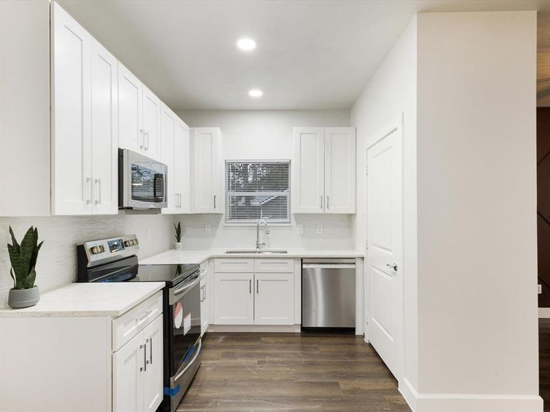Kitchen featuring appliances with stainless steel finishes, white cabinetry, dark wood-type flooring, tasteful backsplash, and recessed lighting