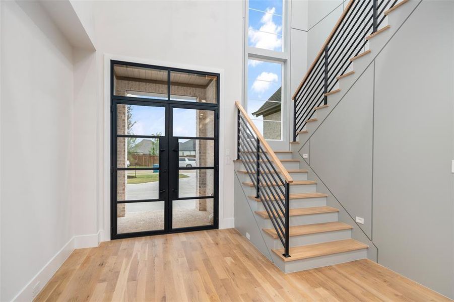 Grand entry showcasing soaring ceilings, dramatic natural light, and striking wrought iron and glass front doors. Real hardwood floors flow seamlessly throughout both levels, while the modern staircase with black iron railing and wood treads creates a stunning architectural focal point.