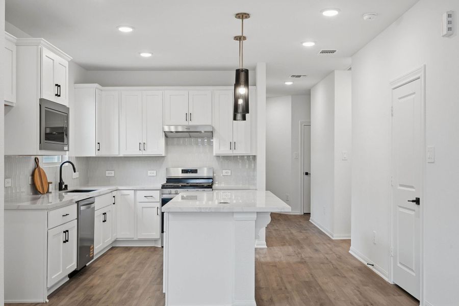 A spacious island anchors the kitchen, surrounded by sleek cabinetry and stainless steel appliances, all opening into a sunlit living space ideal for gathering.