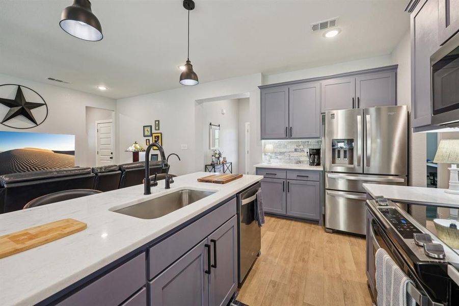 Kitchen with gray cabinetry, stainless steel appliances, light wood-type flooring, backsplash, and decorative light fixtures Kitchen with gray cabinetry, stainless steel appliances, light wood-type flooring, backsplash, and decorative light fixtures