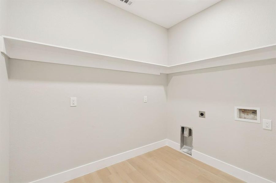Dedicated laundry area featuring light wood-finish flooring, white baseboards, and built-in shelving Dedicated laundry area featuring light wood-finish flooring, white baseboards, and built-in shelving