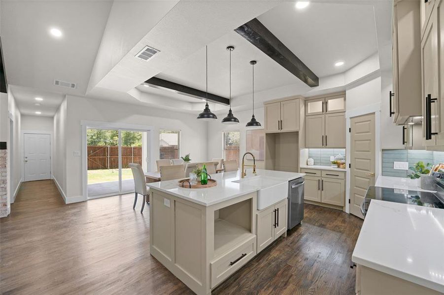 Kitchen featuring a central island with a farmhouse sink, stone countertops, pendant lighting, and wood-finish flooring Kitchen featuring a central island with a farmhouse sink, stone countertops, pendant lighting, and wood-finish flooring