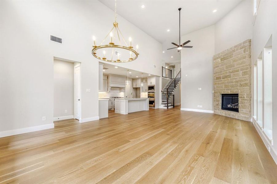 Unfurnished living room featuring a high ceiling, a stone fireplace, light wood-style floors, a ceiling fan, and a chandelier