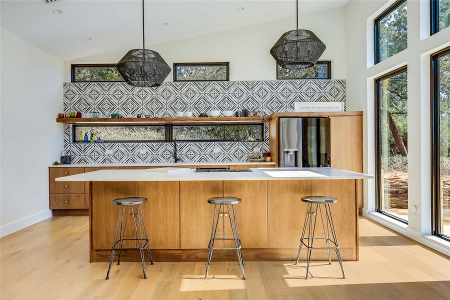 Kitchen with light countertops, light wood-style floors, vaulted ceiling, refrigerator with ice dispenser, and brown cabinets