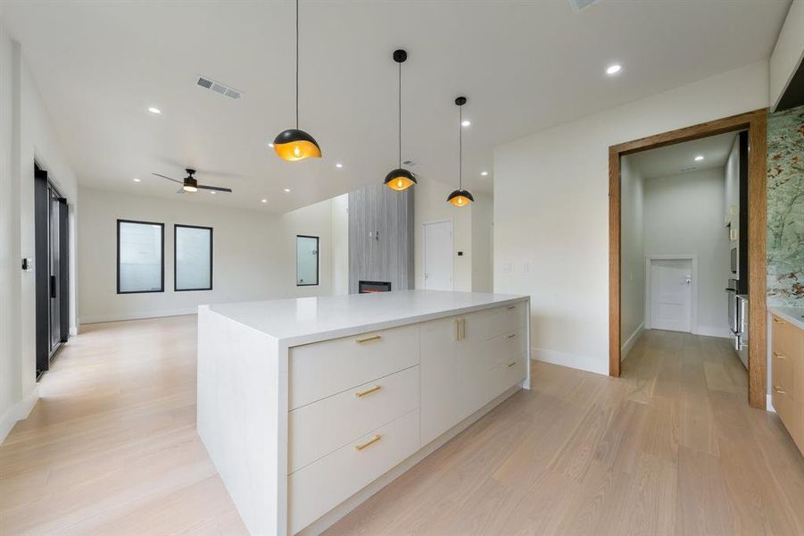 Kitchen featuring modern cabinets, hanging light fixtures, light wood-style flooring, a center water fall quartz island, and white cabinets