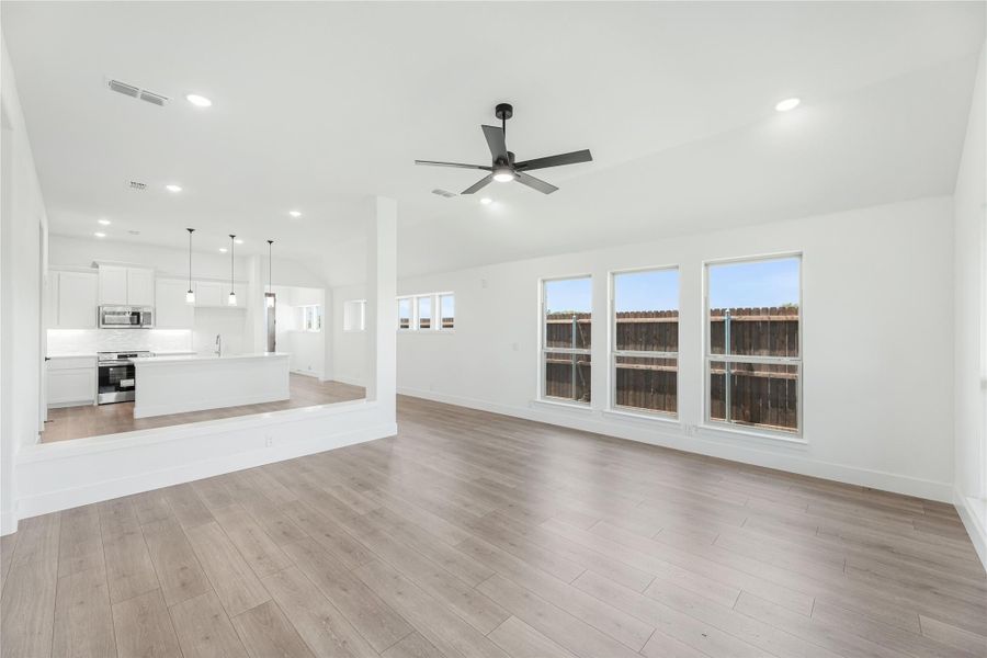Open living area with hardwood floors and ceiling fan, open to white kitchen with island and pendant lights