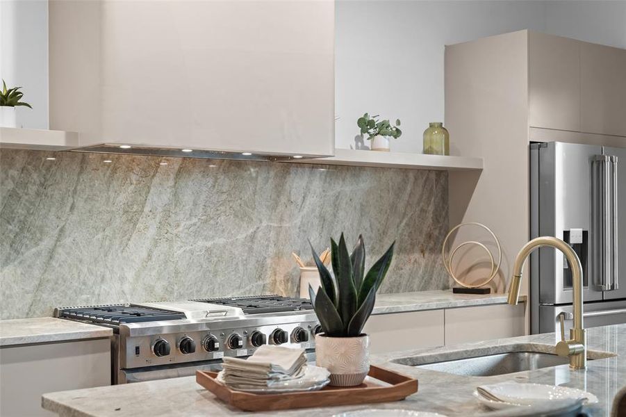 Kitchen view of custom range hood, tasteful backsplash, stainless steel appliances, light stone counters, and modern cabinets