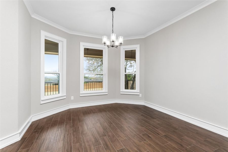 Spare room with a chandelier, dark wood-style floors, baseboards, and ornamental molding Spare room with a chandelier, dark wood-style floors, baseboards, and ornamental molding