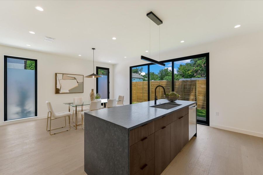 Kitchen with modern cabinets, light wood-style floors, a large island with sink, recessed lighting, and dark countertops