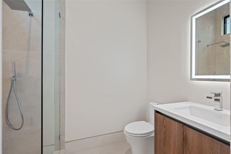 Sleek modern bathroom with glass-enclosed shower, vanity, and illuminated LED mirror. Sleek modern bathroom with glass-enclosed shower, vanity, and illuminated LED mirror.