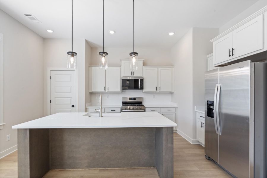 Kitchen featuring an island with countertop, stainless steel appliances, white cabinetry, pendant lighting, and wood-finish flooring Kitchen featuring an island with countertop, stainless steel appliances, white cabinetry, pendant lighting, and wood-finish flooring