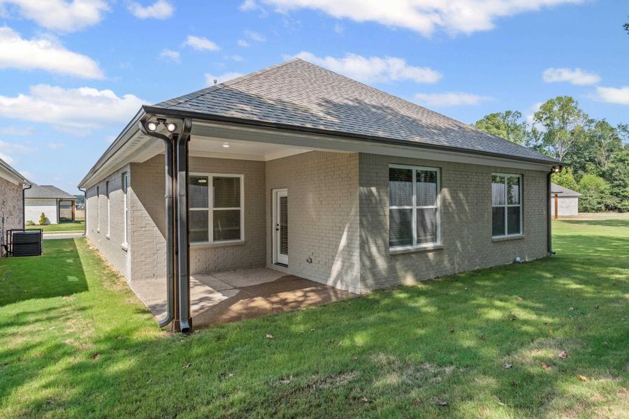 Rear view of property with a lawn, a patio, brick siding, and a shingled roof