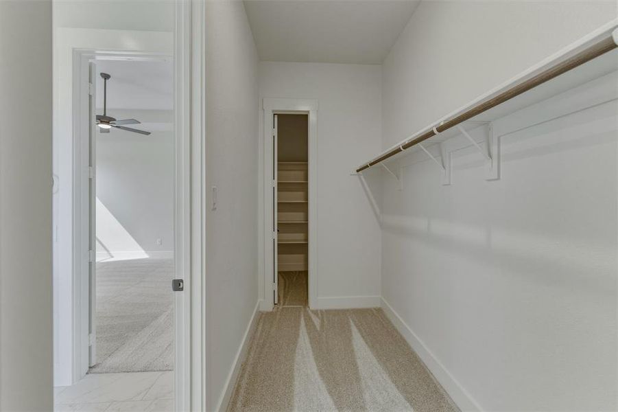 Walk-in closet featuring white wire shelving, a wood-finish hanging rod, and light-toned carpet flooring Walk-in closet featuring white wire shelving, a wood-finish hanging rod, and light-toned carpet flooring