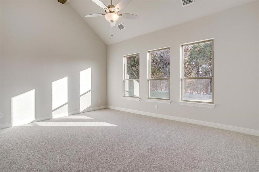 Carpeted empty room featuring ceiling fan and high vaulted ceiling