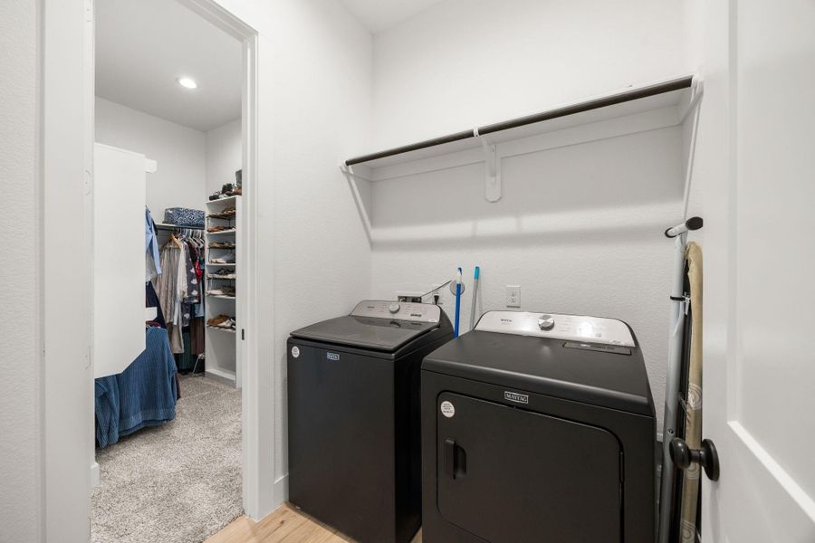 The utility space includes upper hanging storage and full-size washer and dryer connections, conveniently located near the primary suite.
