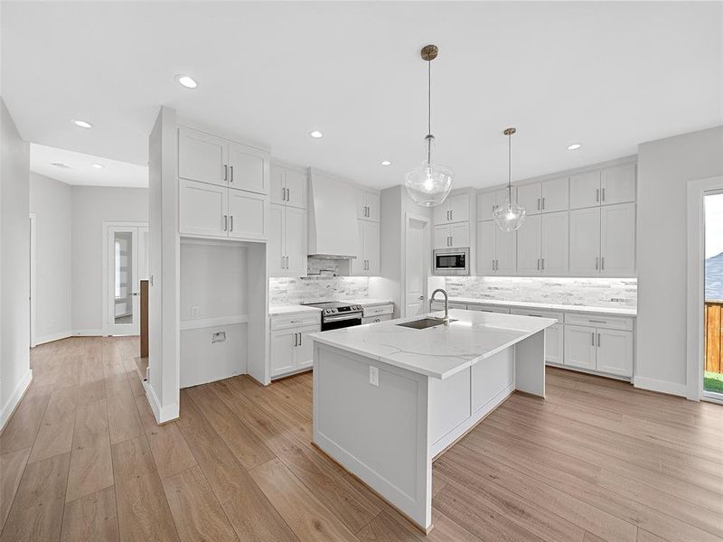 Kitchen featuring sink, appliances with stainless steel finishes, light hardwood / wood-style flooring, custom exhaust hood, and an island with sink