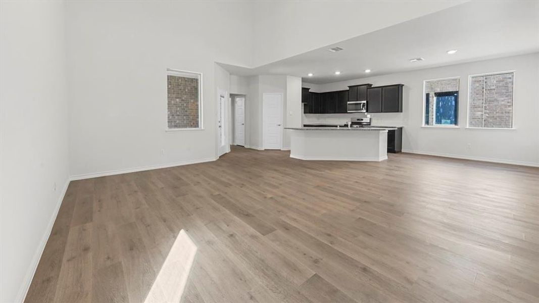 Unfurnished living room with light wood-type flooring, recessed lighting, and a towering ceiling