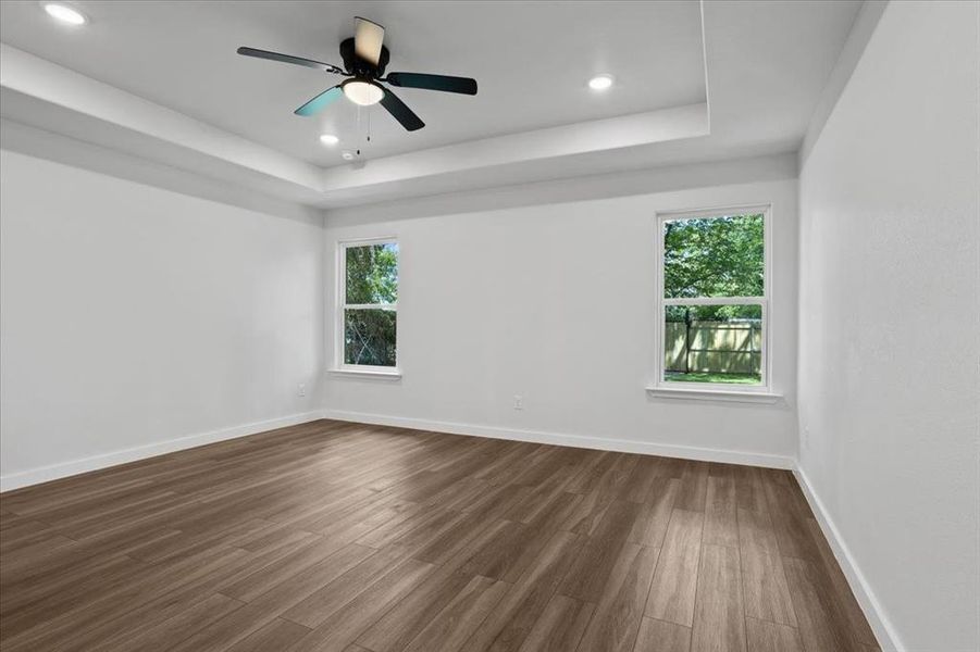 Spare room with a tray ceiling, ceiling fan, wood-type flooring, and a wealth of natural light