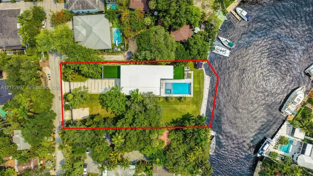 Waterfront property featuring a private dock, rectangular swimming pool, expansive lawn, and paved driveway