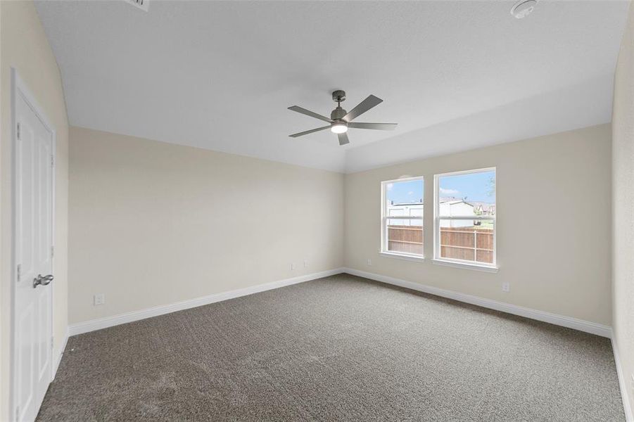 Spacious room featuring neutral carpeting, light beige walls, and a vaulted ceiling with a modern ceiling fan