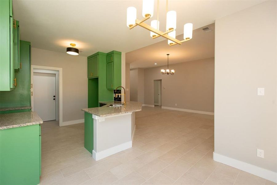 Kitchen with sink, green cabinetry, pendant lighting, light stone counters, and light tile floors