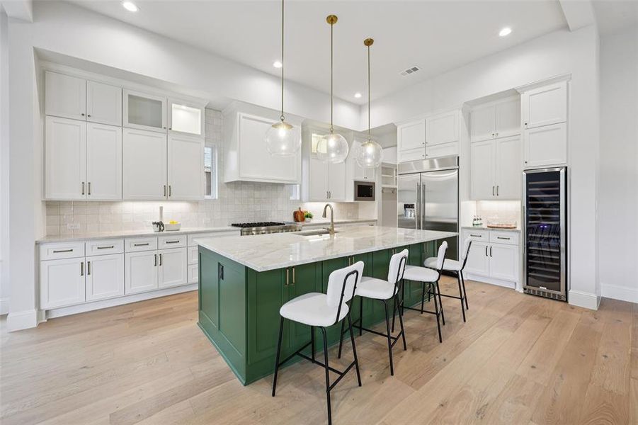 Two tone kitchen with two tone cabinetry, a center island with sink, decorative light fixtures, beverage cooler, and glass insert cabinets