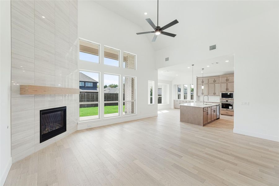 Open-concept living room with tile fireplace, high ceilings, and hardwood floors open to kitchen with island